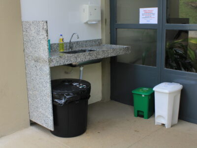 Pia de lavagem de utensílios com apoio de três lixeiras, preta, verde e branca, para resíduos, recicláveis, orgânicos e rejeitos, respectivamente.