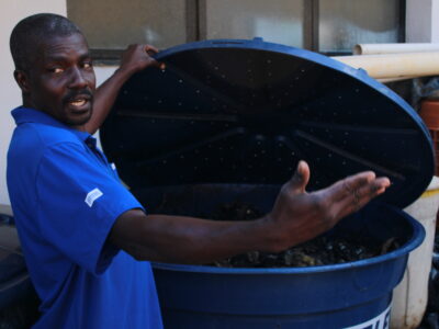 Colaborador com a tampa da composteira aberta, explicando as etapas do processo.
