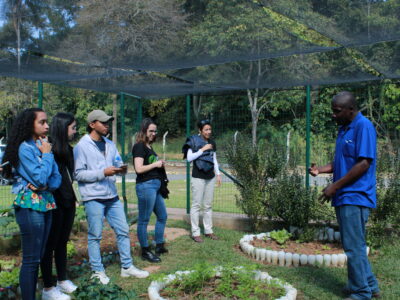 Estudantes se posicionam dentro da Horta Orgânica ouvindo explicações sobre o projeto.